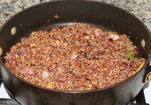 Red quinoa cooking in pot with onion, chilies, ginger and spices